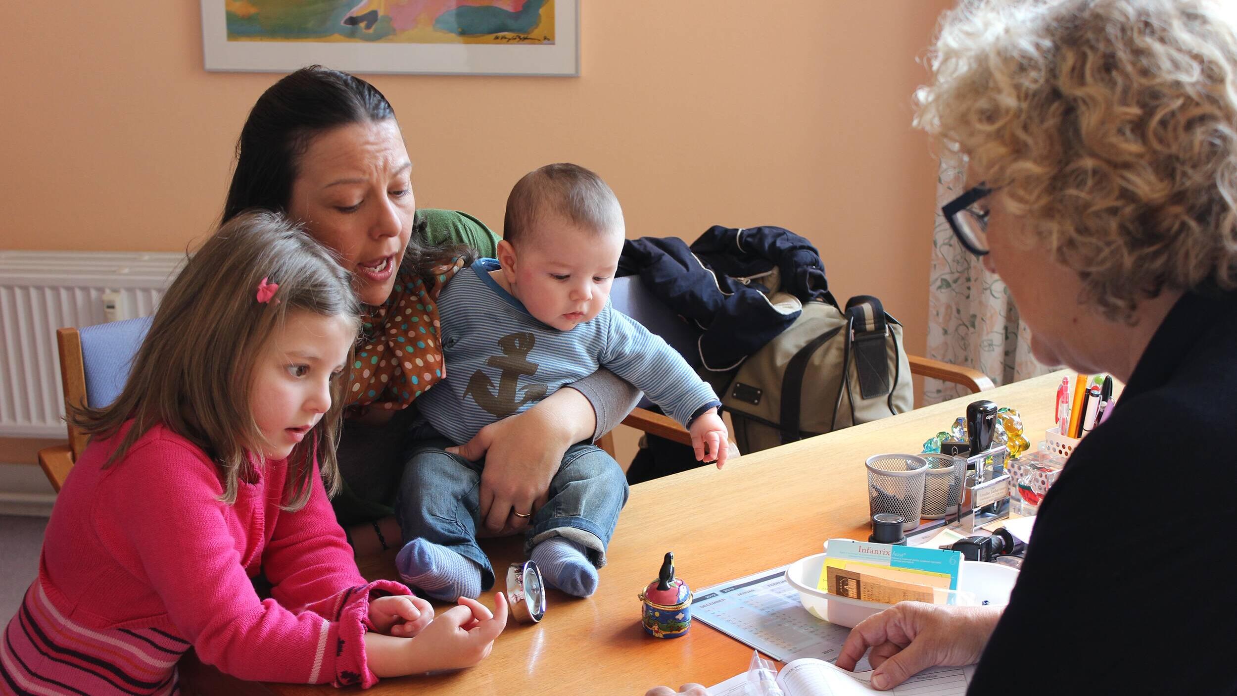 A doctor explaining vaccination procedures to a mother with her two young children.