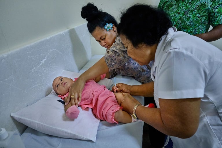 A baby is vaccinated by a nurse while her mother holds the baby's arms.